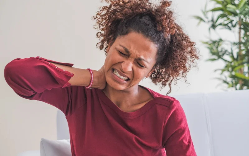 Woman experiencing neck and shoulder pain, Modern Movement Medicine treatment.