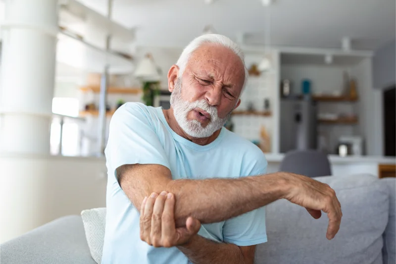 Older man experiencing elbow pain and discomfort in a home setting.