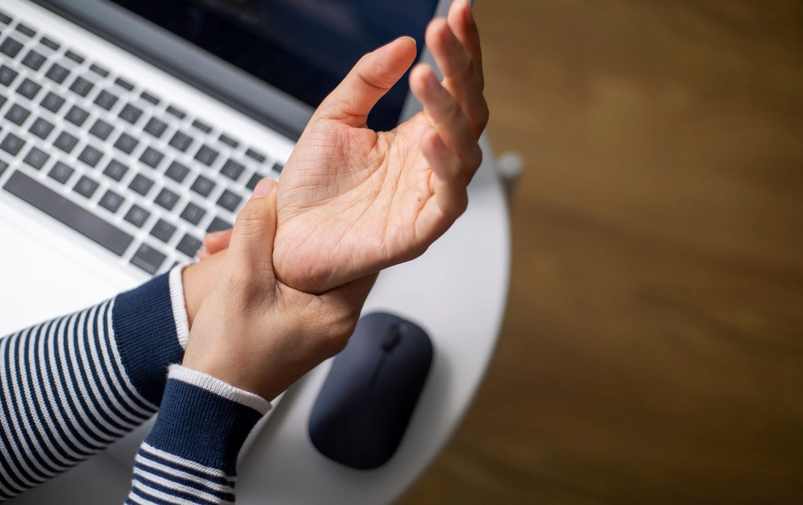 Hand experiencing wrist pain near laptop and mouse illustrating nerve irritation and repetitive stress.