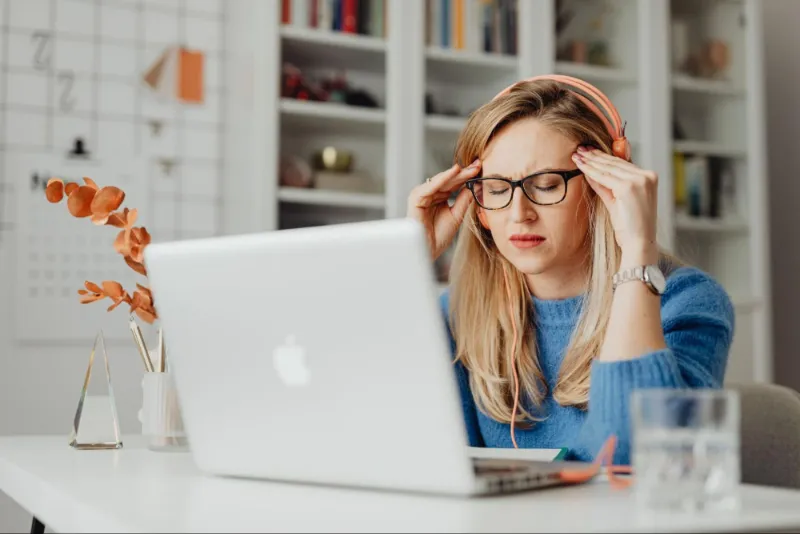 Woman experiencing headache and migraines at laptop, Modern Movement Medicine treatment.
