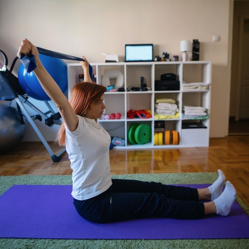 Woman performing stretching exercises with resistance band for rehabilitative therapy at home.