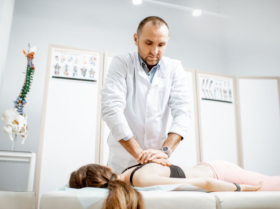 Chiropractor examining patient's spine and posture with anatomical model and X-rays in background.